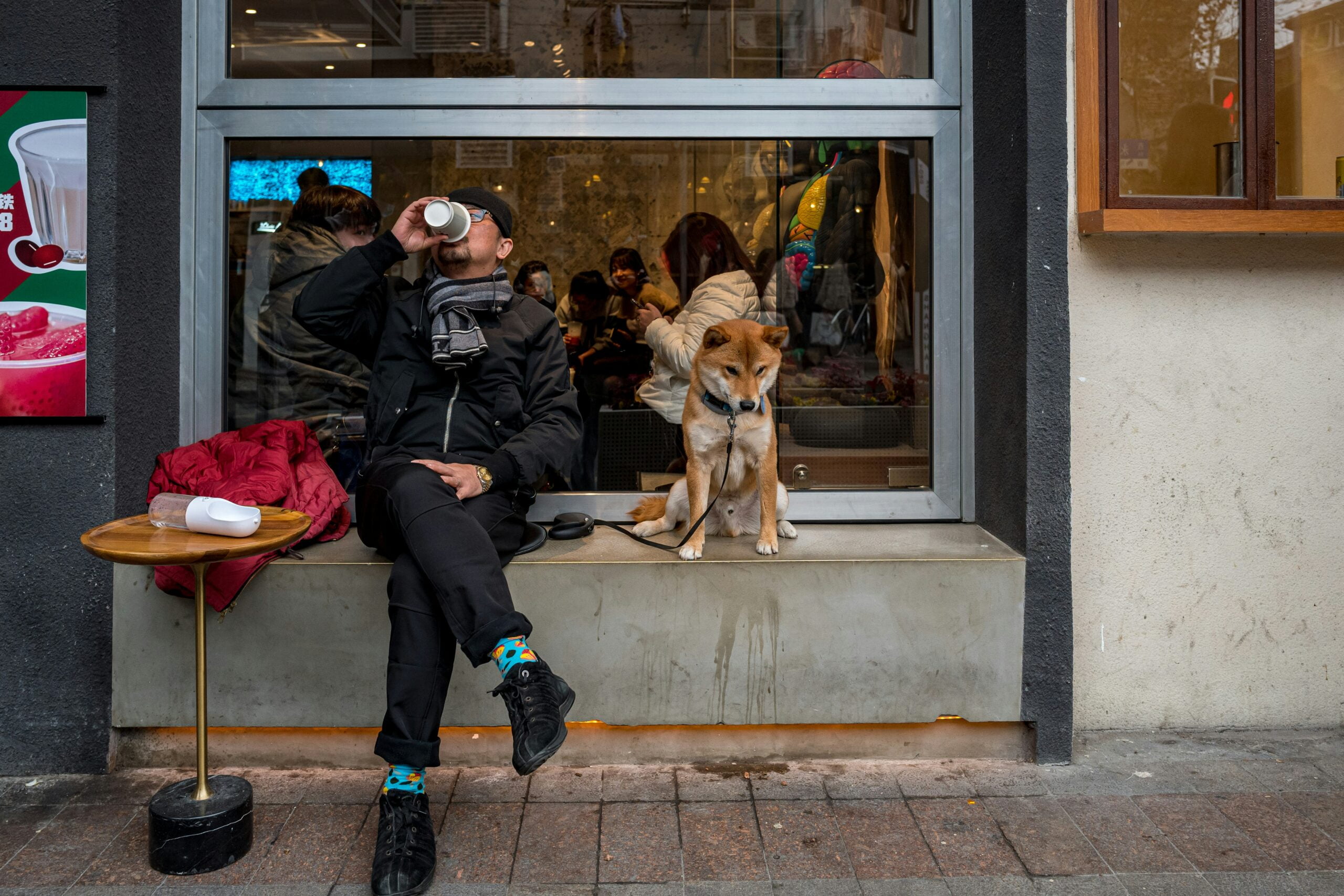 man in black jacket sitting beside brown dog